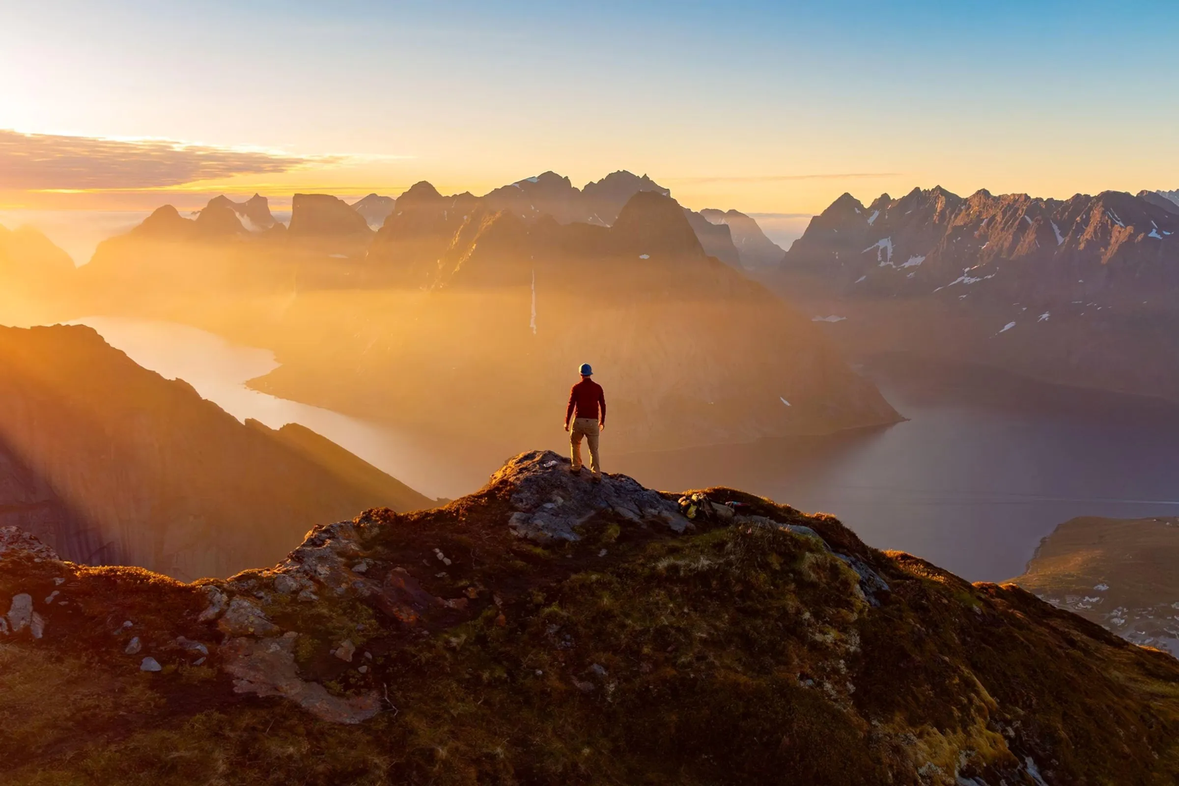 Hiker on a summit overlooking a fjord and mountains in late-afternoon sun